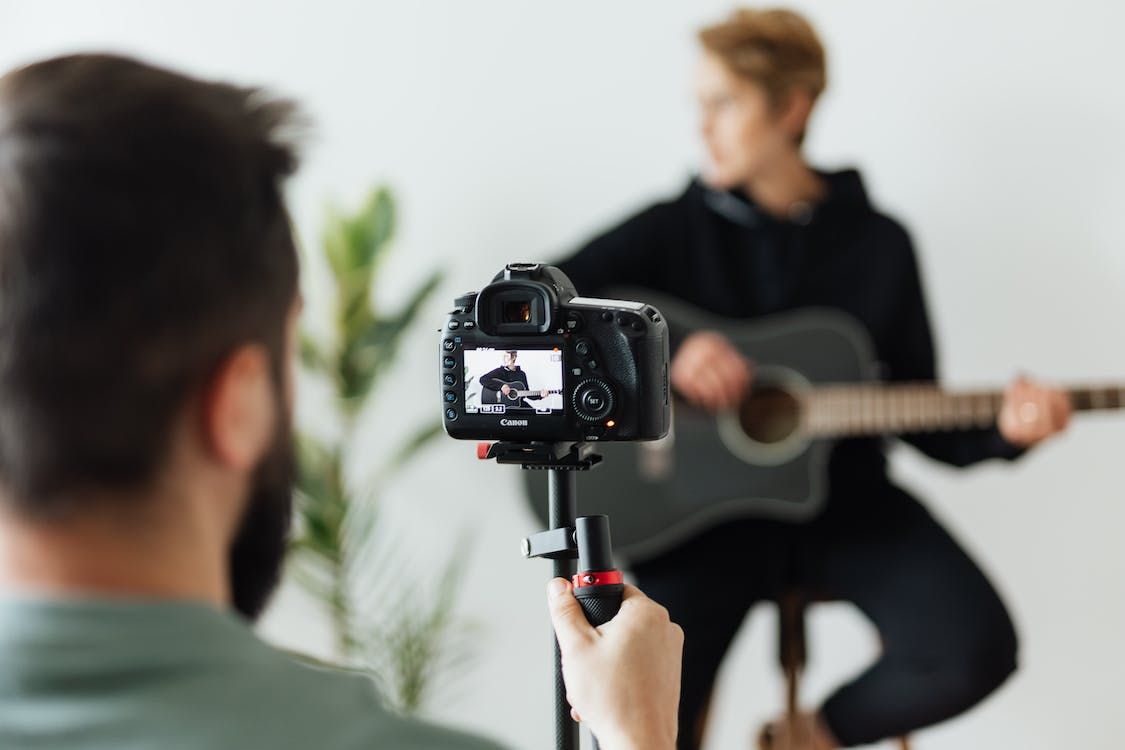 image showing a man filming someone playing the guitar with a video camera setup