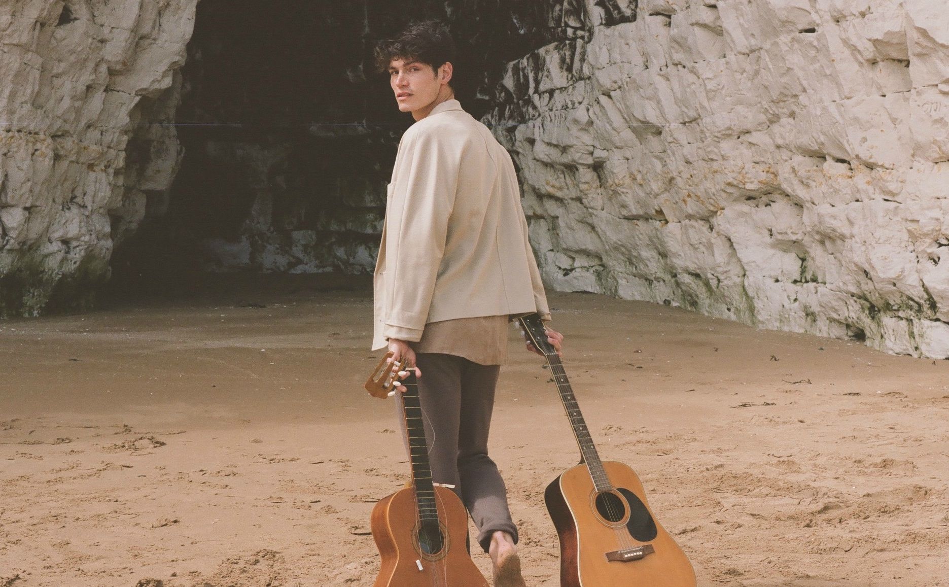 image of a man dragging two guitars along the beach by Lauren Luxenberg