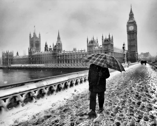 black and white image of a man with an umbrella walking on a snowy street by Big Ben by Ronya Galka