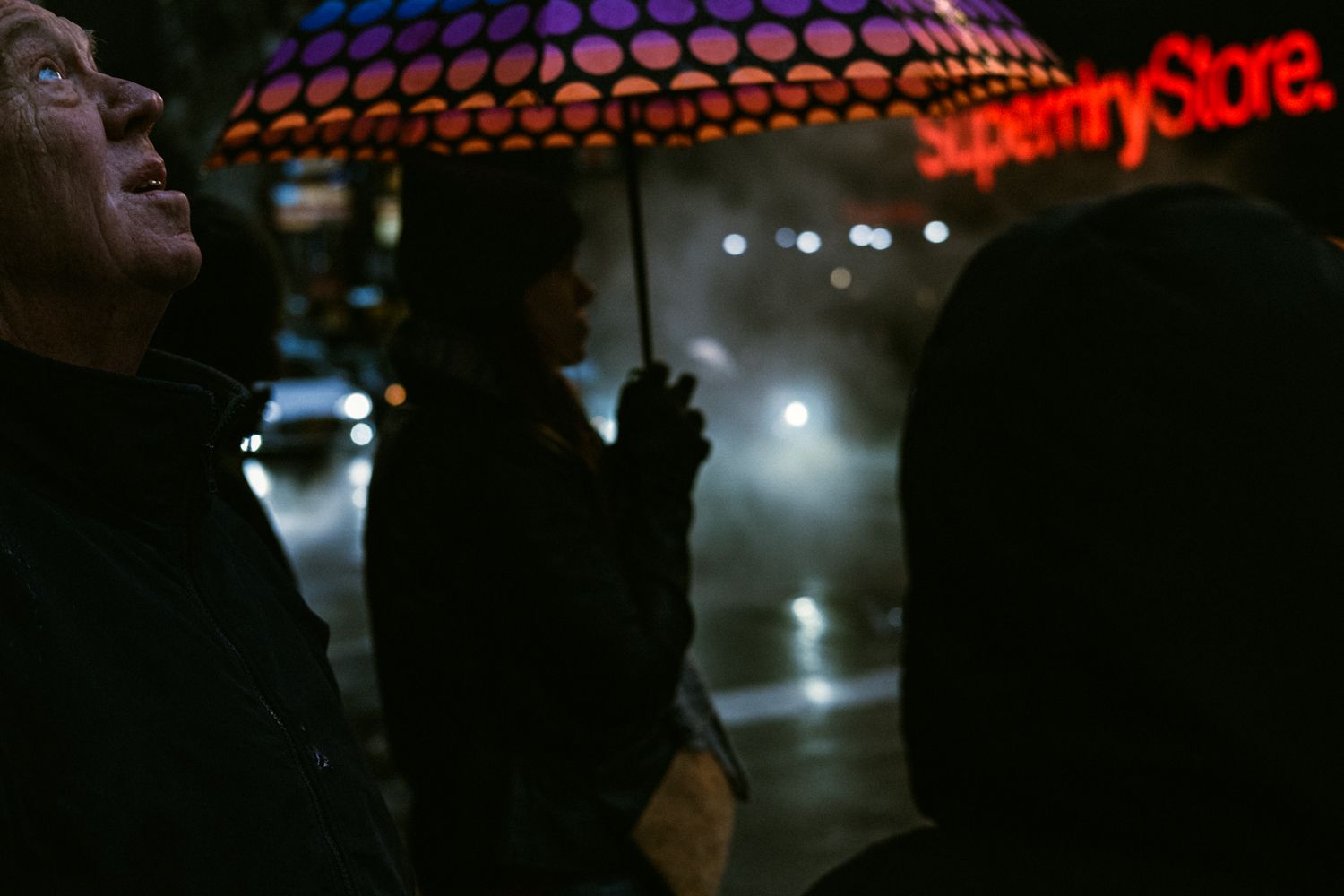 image of a man looking up against a dark background with a store sign lit up in neon red by Joshua K Jackson