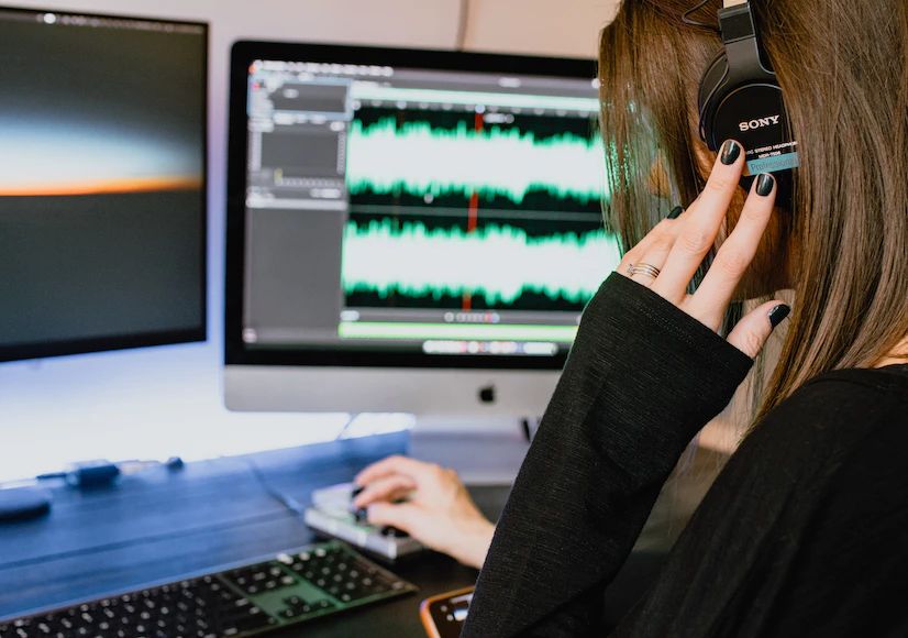 image of a woman using audio production software on a computer in a home recording studio