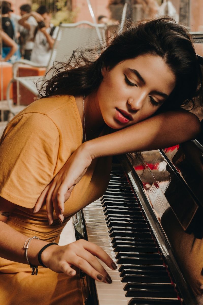 woman sitting on a stool, leaning on a piano and playing