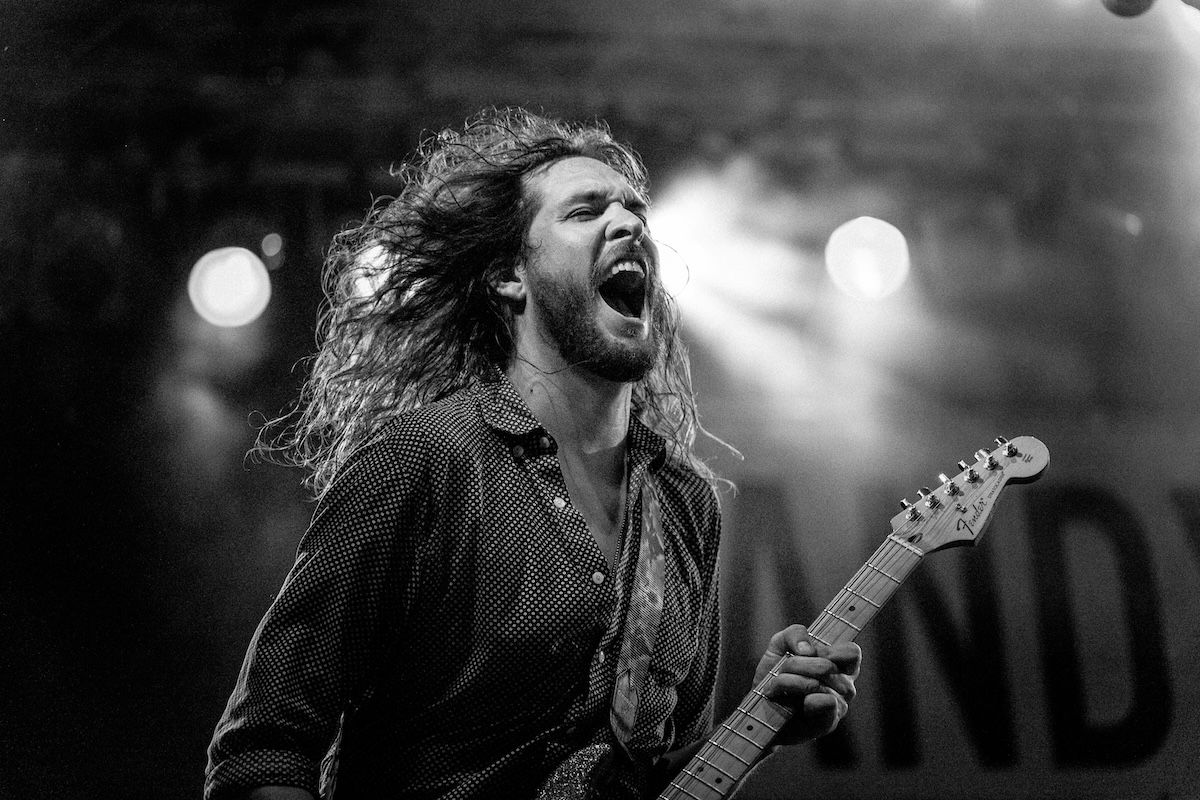 man with long hair playing guitar on stage