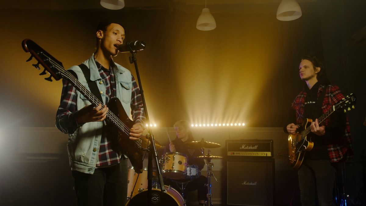 three men in a band playing guitar, bass guitar and drums on stage 