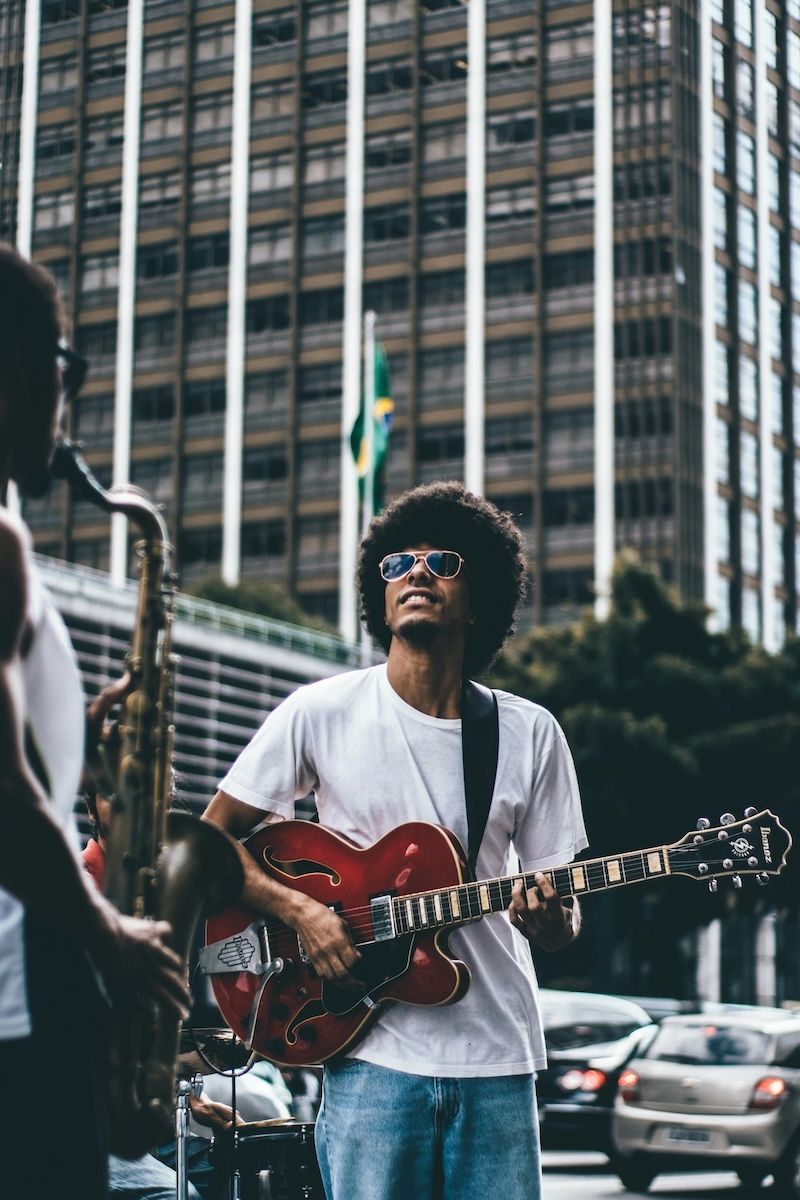 man standing on a street playing jazz guitar next to a man playing saxophone 