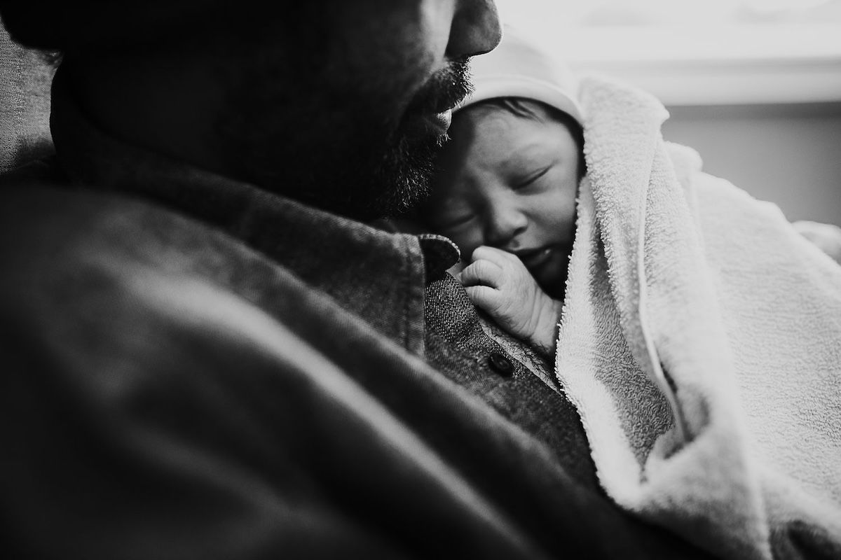 A closeup of a father holding his newborn baby on his chest with a towel wrapped around the baby