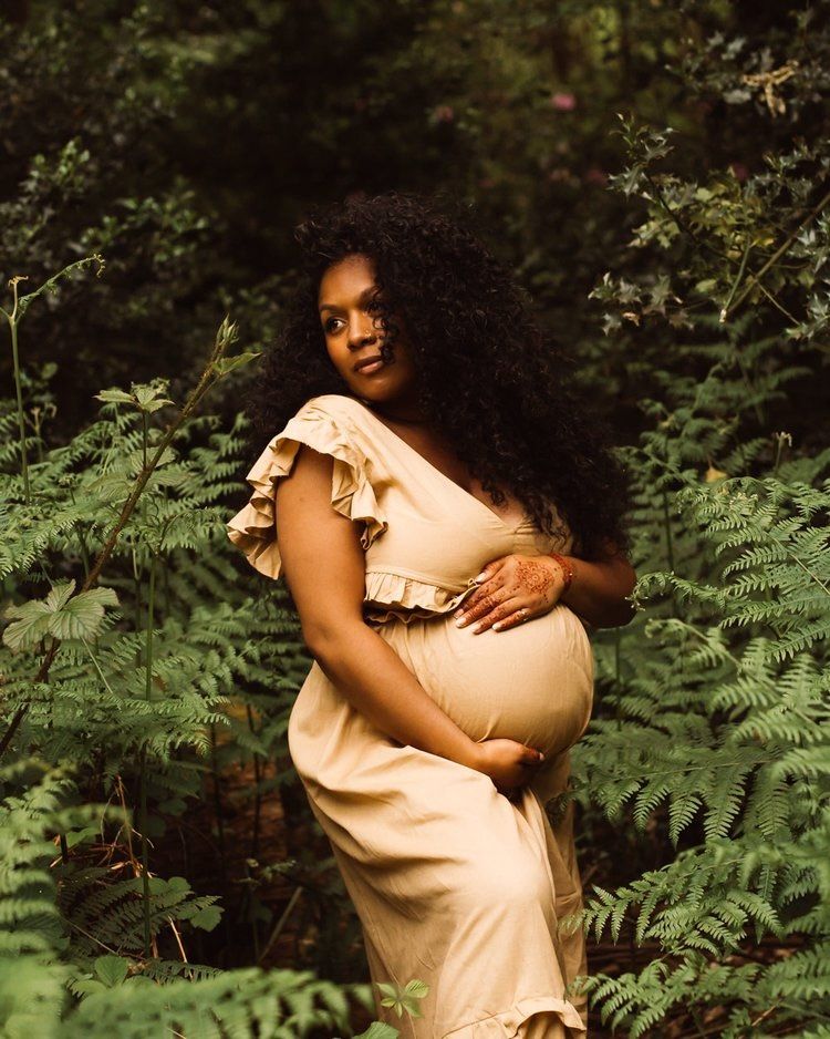 an outdoor maternity shoot, the woman wears a dress and poses in the forest 