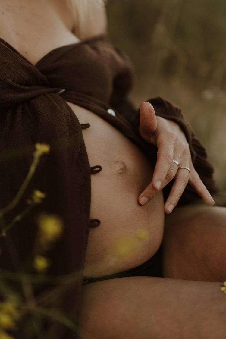 close up of pregnant woman's left hand on her stomach as she sits outdoors